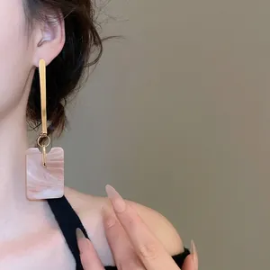 Minimalist square marble pendant earrings with gold accents shown on a model