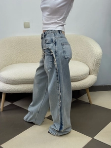 Detail of frayed fringe seams on side of high-waisted light blue wide-leg denim jeans