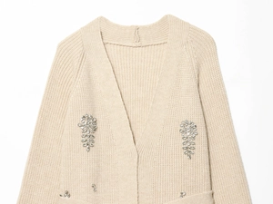 Gros plan d'un gilet en maille beige avec des ornements en strass en forme de feuille