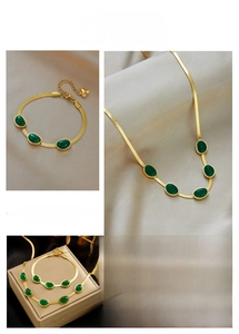 Detailed macro of gold snake chain set with emerald green stones on silk background