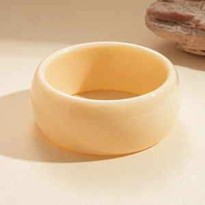 Detail view of a thick cream acrylic round bangle on a natural stone surface