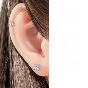 Macro shot of silver flower earrings with blue cubic zirconia on cartilage piercings