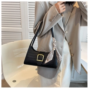Detail of black crocodile pattern baguette bag with golden buckle and geometric silk scarf