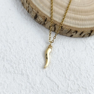 Close-up of golden Italian horn pendant on wood block with polished finish