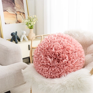 Detail of a round pink floral throw pillow with decorative ruffles on a stylish chair