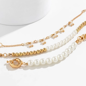 Detailed macro view of triple-layered gold chain and pearl bracelets with spring clasp