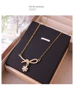 Detailed view of gold bow and floral pendant necklace with micro-pave crystals