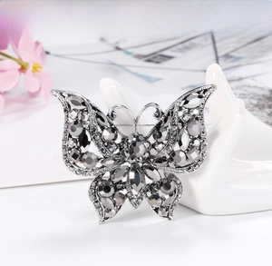 Detail view of a vintage butterfly brooch with grey rhinestones on a ceramic hand display