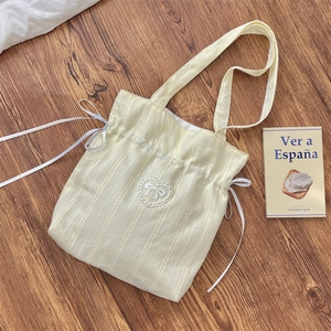 Dettaglio borsa tote plissettata gialla con ricamo a fiocco bianco su legno