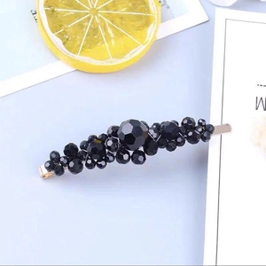 Macro shot of stylish black beaded hair clip with gold metal base on light purple background