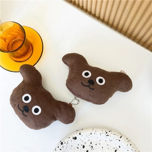 Detail of cute brown plush dog head purses with metal chain pendants on white table