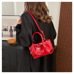 Detailed view of red glossy leather pleated dumpling bag worn with a long black coat