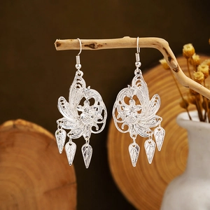 Ethnic style silver hollow flower earrings with leaf tassels on a rustic branch stand