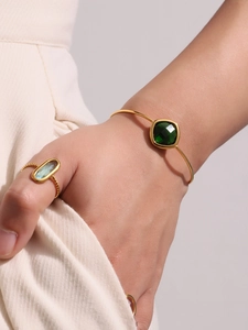 Detail of gold open bangle with square green gemstone and twisted rope blue stone ring