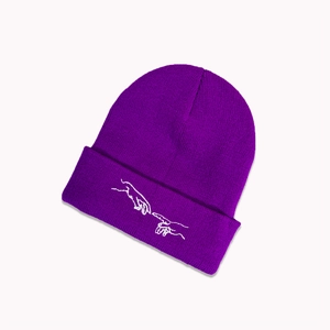 Gros plan du bonnet en tricot violet avec broderie blanche de mains sur le revers