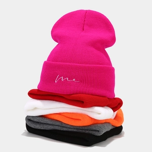 Stack of colorful knit beanies with me embroidery in red, pink, grey and black colors