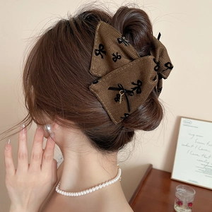 Detail of dark brown tweed bow hair claw with metal charm on hair with elegant vibes