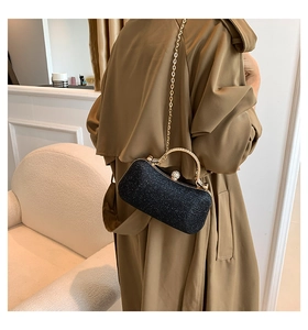 Detail of black sequined crossbody bag with gold chain and pearl clasp on a trench coat