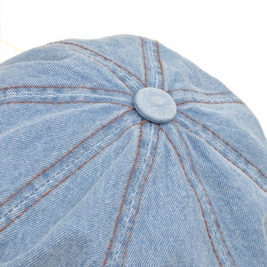 Macro detail of washed denim newsboy cap showing top button and contrast stitching