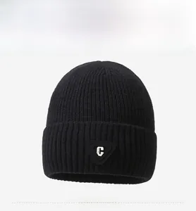 Detail of black ribbed knit beanie featuring a minimalist white letter C triangle patch