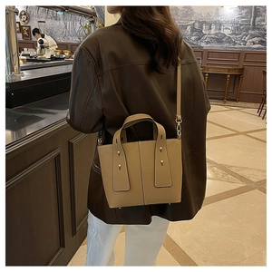 Brown litchi leather bucket bag shown on a model in a cafe, featuring gold stud details