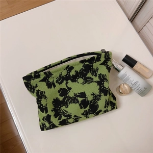 Detailed top view of a green floral jacquard makeup bag with black zipper and accessories