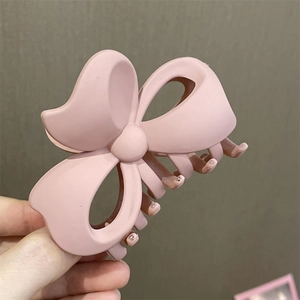 Primer plano de una pinza de pelo mariposa rosa mate grande sostenida frente a una pared