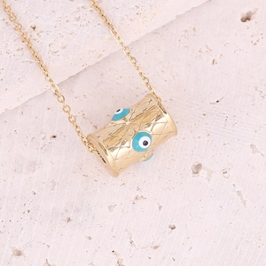 Detailed shot of gold cylinder pendant with evil eye patterns on textured stone surface