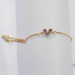 Detailed close-up of a golden heart bracelet with purple cubic zirconia stones