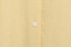 Macro shot of high-quality pale yellow cotton-linen fabric with a white resin button