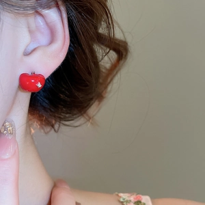 Close-up of red apple stud earrings with leaf detail worn on a female model side profile