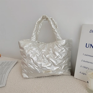 Close-up of pearl white quilted handbag featuring intricate bow textures and fabric label