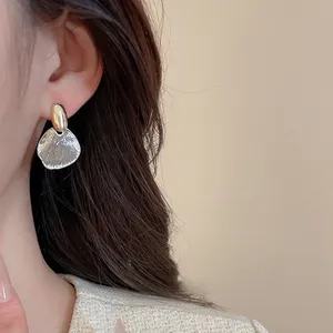 Close-up of elegant mixed-metal fan-shaped earrings worn with chic tweed jacket