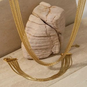 Elegant multi-layer gold tassel necklace displayed on a minimalist stone background