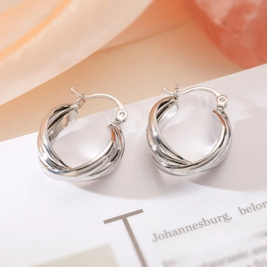 Minimalist silver twisted geometric hoop earrings displayed on a vintage paper background