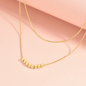 Minimalist double-layer necklace with eight polished gold beads on a soft pink background
