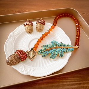 Detail of vintage necklace set with crystal leaf and acorn charms on a ceramic plate