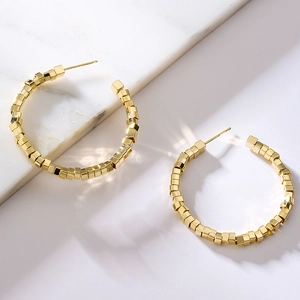Golden geometric hoop earrings made of small cubes on a white marble surface