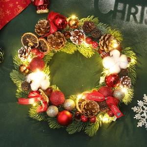 Christmas pine needle wreath with red gold balls pinecones and LED lights on green background