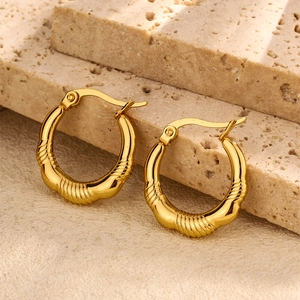 Close-up of textured gold-tone stainless steel hoop earrings on a beige stone
