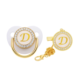 Detailed close-up of a golden pacifier and clip with rhinestone-encrusted letter D design