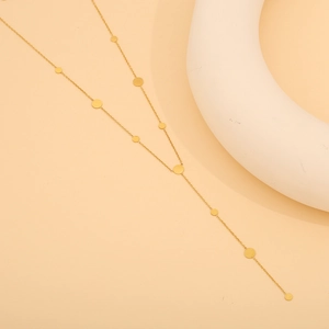 Close-up of golden Y-shaped long necklace with minimalist round disk pendants on modern display