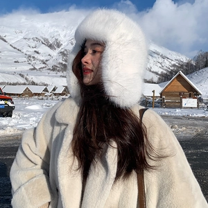 Detail of white faux fur winter hat and plush coat against a snowy mountain background