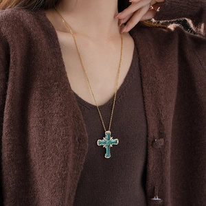 Detailed close-up of a zircon cross pendant necklace with green gemstone on a gold chain