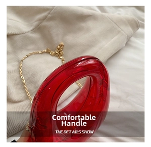 Close-up of red transparent acrylic evening bag with gold chain and curved handle
