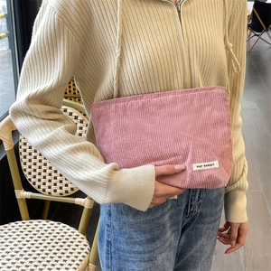 Pink corduroy makeup bag with hand strap, minimalist pouch shown in street style cafe setting