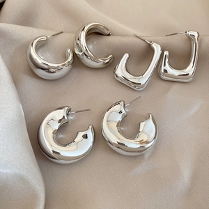 Detail of three pairs of silver geometric stud earrings on a beige silk fabric