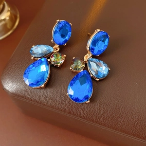 Detailed view of vintage gold earrings with blue teardrop crystals on brown leather