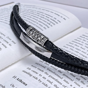 Close-up of black braided leather men's bracelet with silver metal bars on book