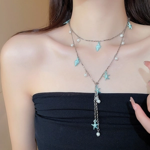 Détail d'un collier à pompons bleu avec étoile de mer et perles sur tenue noire